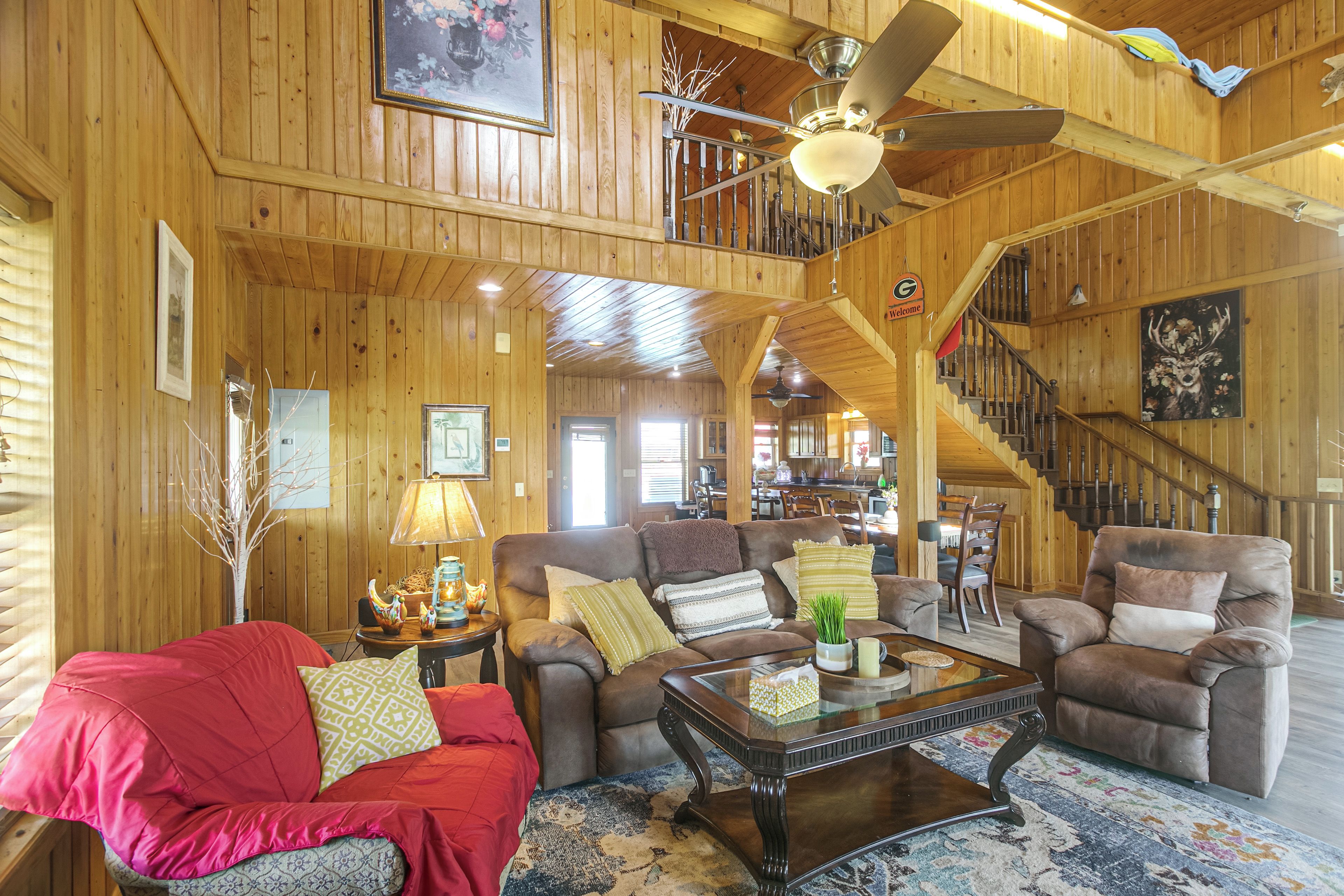 A spacious living room with a high ceiling, wooden walls, a staircase, and a dining area.