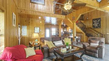 A spacious living room with a high ceiling, wooden walls, a staircase, and a dining area.