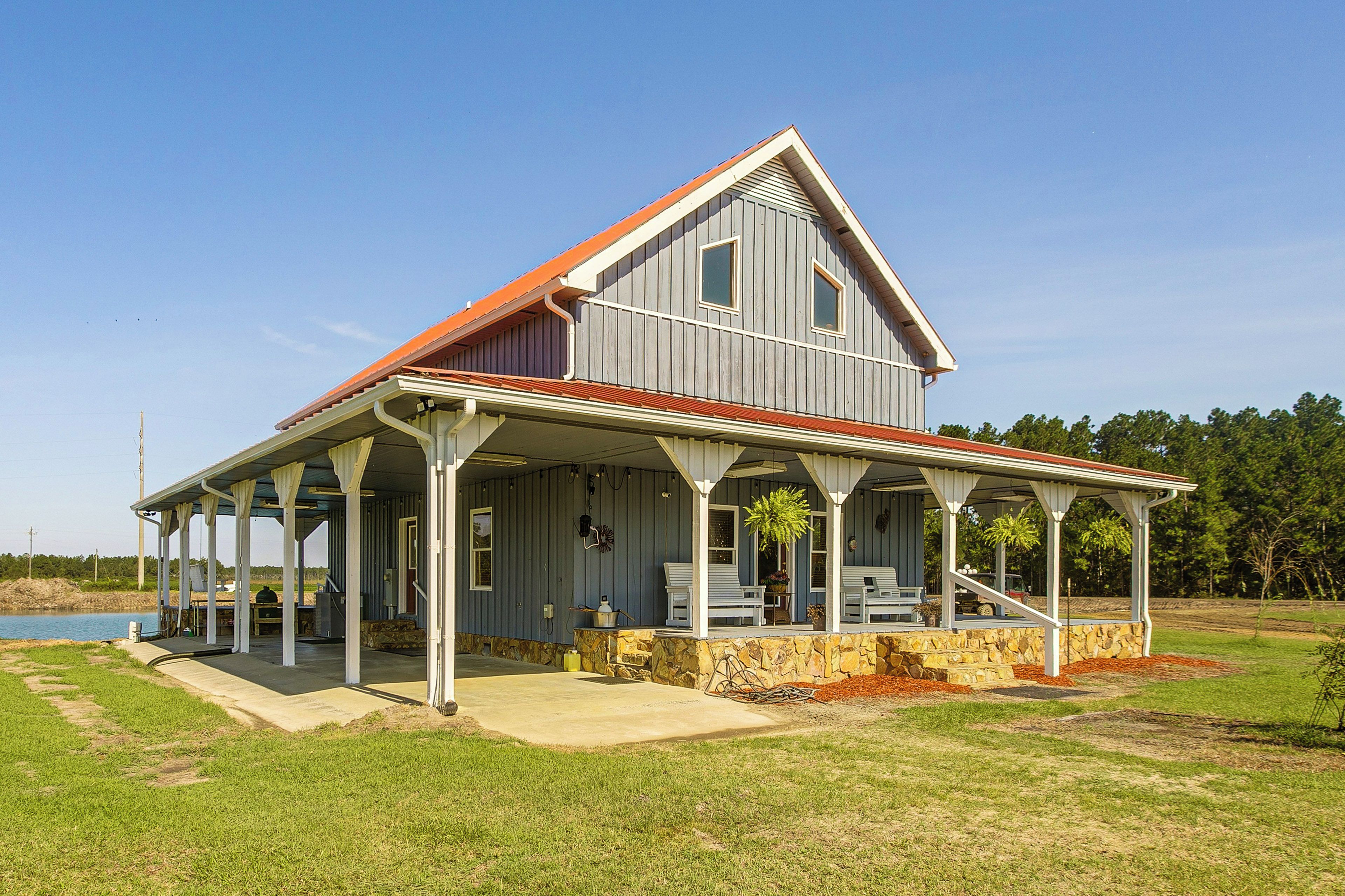 A two-story house with a porch, a stone foundation, and a view of a body of water.