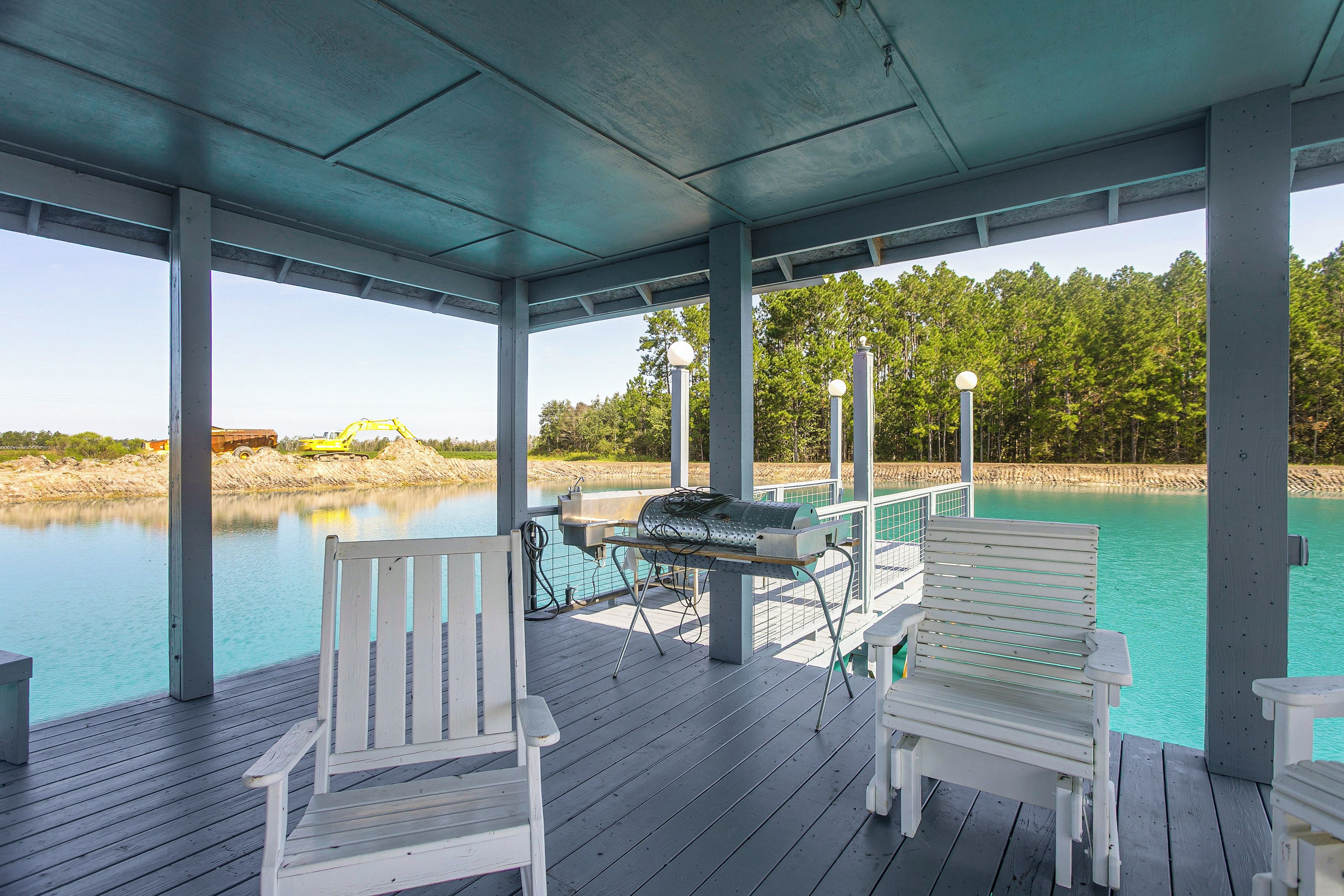 A covered outdoor area with a pool, two white Adirondack chairs, a grill, and a view of a forested area.