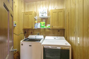 A compact laundry room with wooden walls, a washing machine, a dryer, and a shelf with cleaning supplies.