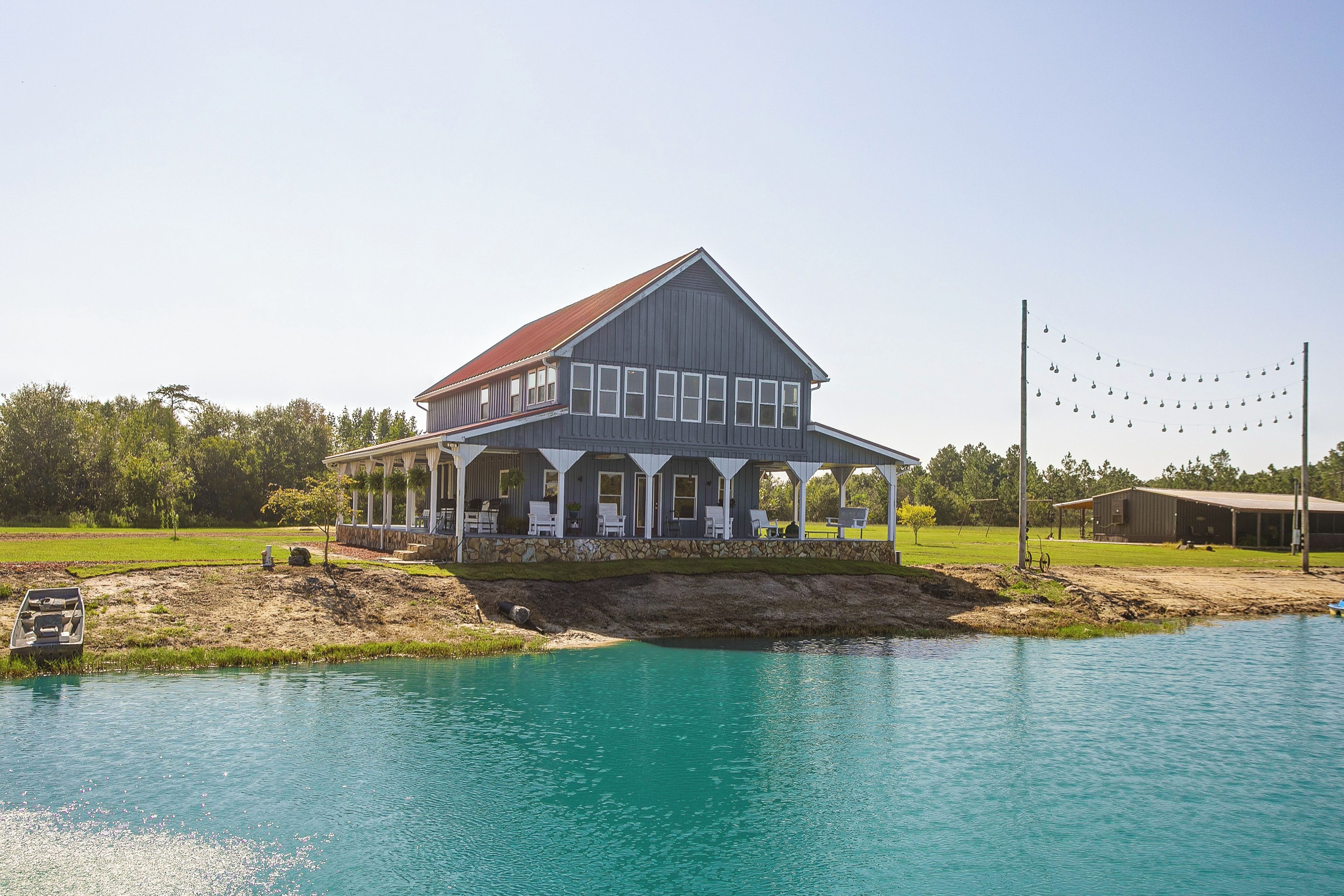 A large two-story house with a porch, a swimming pool, and a dock extending into the water.