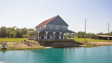 A large two-story house with a porch, a swimming pool, and a dock extending into the water.