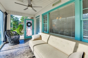 A room with a ceiling fan, a sofa, a wicker chair, and a door with a wreath.