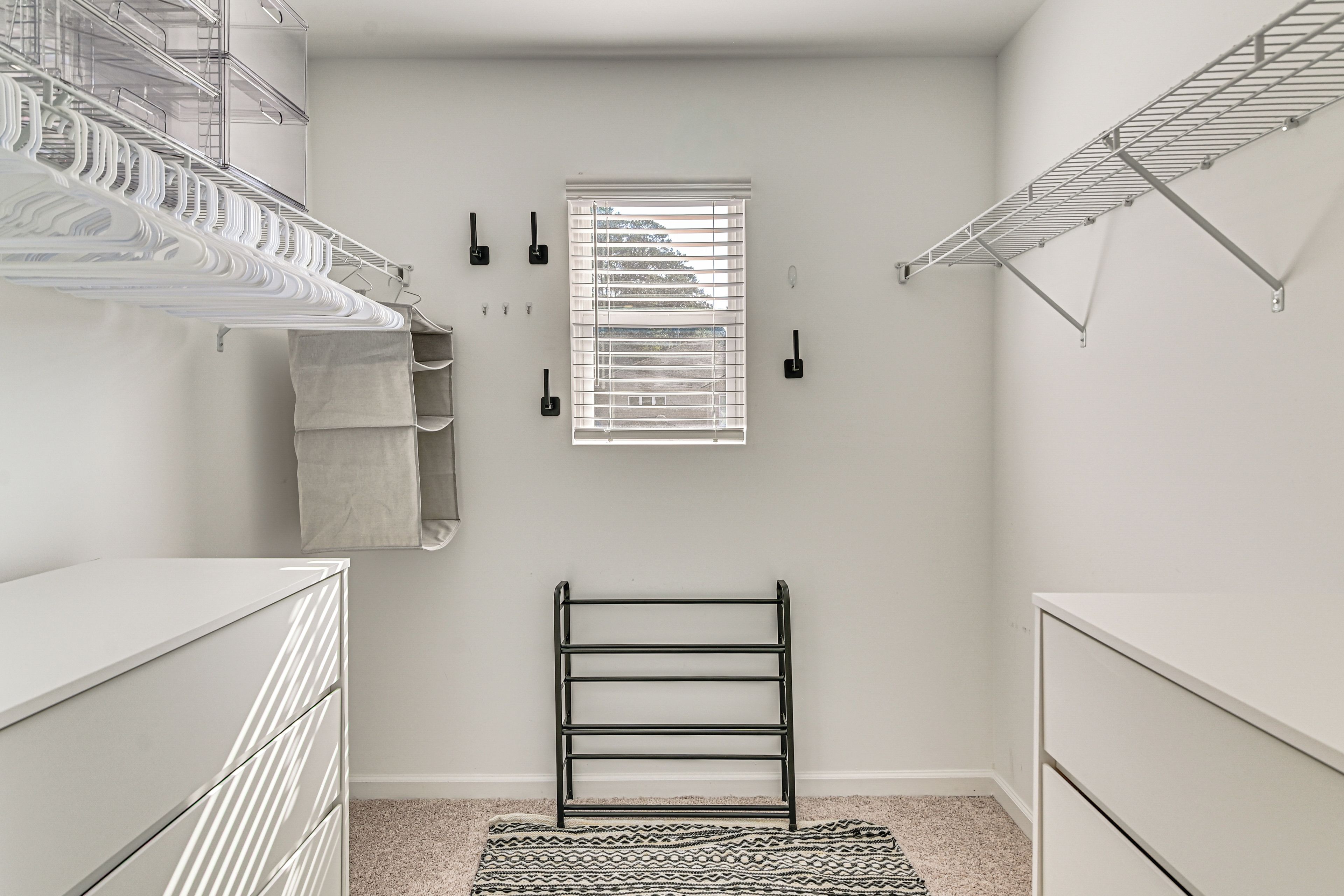 A compact walk-in closet with metal shelving, a drying rack, and a window.