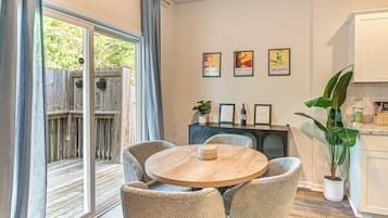 Un comedor con una mesa de madera redonda, cuatro sillas tapizadas y vistas a una terraza de madera a través de puertas de vidrio.
