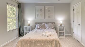 A bedroom with a bed, two bedside tables, a window with curtains, and two wall-mounted artworks.
