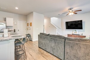 Una cocina moderna con comedor, una sala de estar con televisor grande y una escalera que sube a un nivel superior.