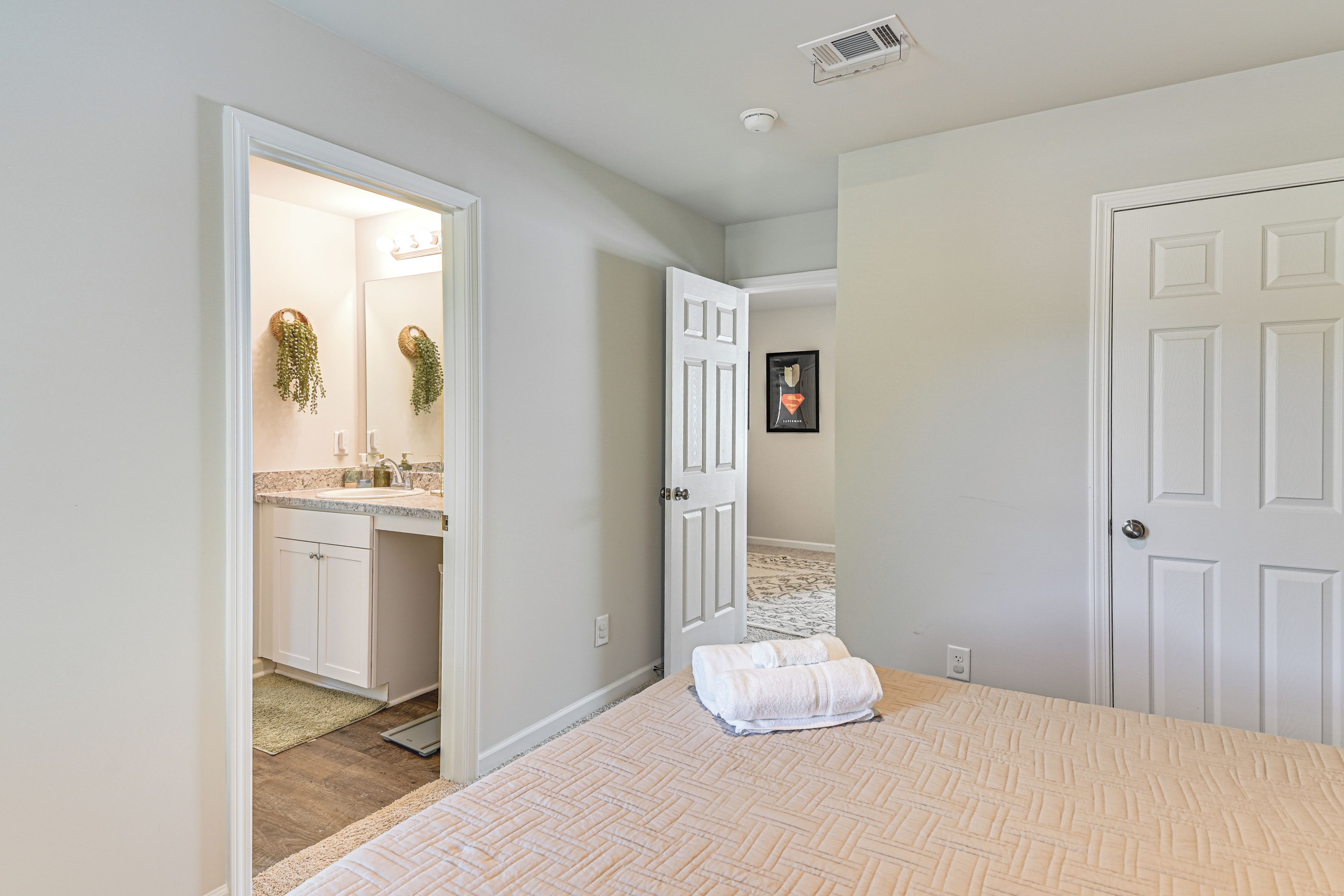 Un dormitorio con cama, una puerta, un baño con lavamanos y un pasillo.