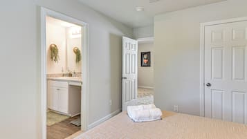 Un dormitorio con cama, una puerta, un baño con lavamanos y un pasillo.
