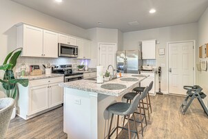 Une cuisine moderne avec des meubles blancs, un îlot central doté de tabourets de bar, des appareils en acier inoxydable et un plancher en bois.