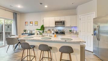 A modern kitchen with a central island, bar stools, stainless steel appliances, and a view to the outside.