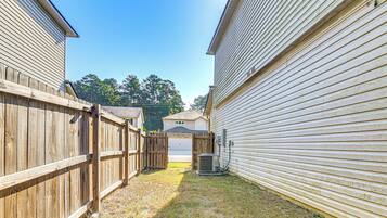 A narrow alleyway between two houses with a wooden fence on one side and a garage door on the other.