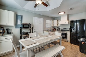 A modern kitchen with white cabinetry, a black refrigerator, and a dining area with a table and benches.