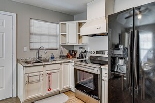 Una cocina con armarios blancos, un refrigerador de acero inoxidable, un horno empotrado y una ventana con persianas.