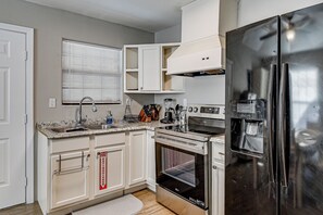 A kitchen with white cabinets, a stainless steel refrigerator, a built-in oven, and a window with blinds.