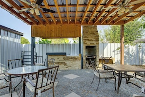 A covered patio area with a stone fireplace, outdoor seating, and a ceiling fan.