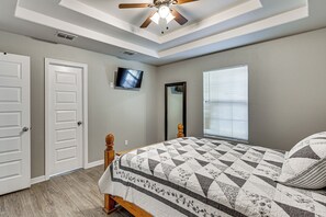 A bedroom with a bed, a ceiling fan, a television, a window with blinds, and a door.
