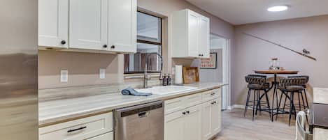 A kitchen with white cabinets, a dishwasher, a bar area with stools, and a fishing rod on the wall.