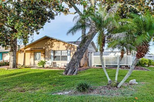 Una casa residencial con césped cuidado, un patio con mobiliario exterior y una palmera.