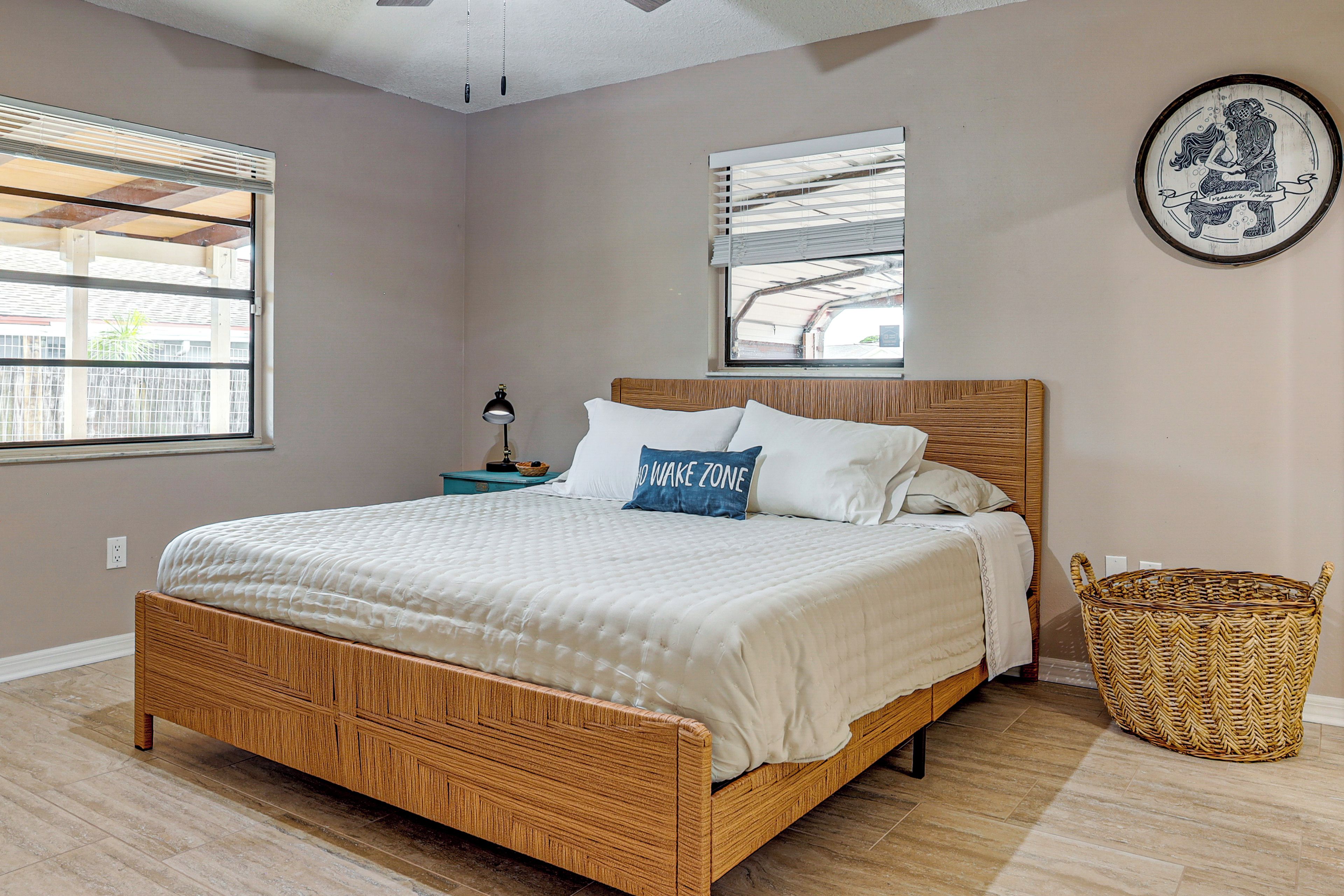 A bedroom with a wooden bed, two windows, a nightstand, a lamp, and a woven basket.