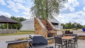 Un'area barbecue esterna con una griglia in pietra, un tavolo con sedie e una zona salotto coperta.