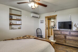 Een slaapkamer met een bed, een dressoir, een stoel, een televisie en een plafondventilator.