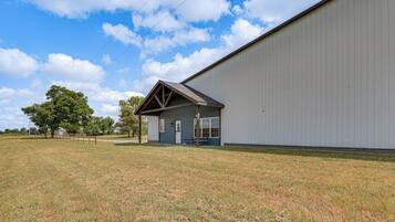 A building with a small attached structure, a grassy field, and a large white wall.