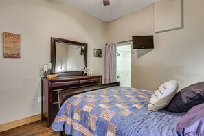 Een slaapkamer met een bed, een dressoir, een spiegel, een televisie en een muur met een poster.