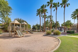Ein Spielplatz mit Rutsche und Klettergerüsten, umgeben von Palmen und einem Poolbereich.