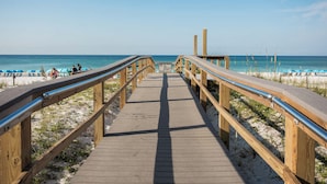 Een houten looppad dat naar een strand leidt, met blauwe parasols en ligbedden.