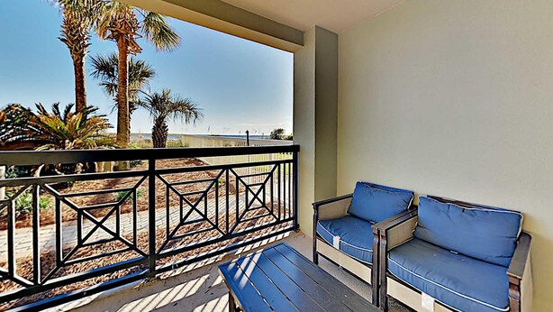 Een balkon met uitzicht op palmbomen en een strand, voorzien van een bank en een tafel.