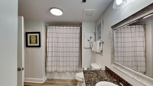 Een badkamer met een wit toilet, een wastafel met een granieten aanrechtblad en een douchegordijn met een ruitpatroon.