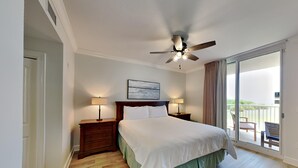 Een hotelkamer met een bed, twee nachtkastjes met lampen, een plafondventilator, een groot raam met uitzicht en een deur.