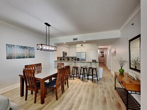 A modern kitchen with white cabinets, a central island, and a dining area with wooden chairs and a table. - Azure #102 | First Floor, Easy Beach Access + Resort Amenities (Fort Walton Beach)