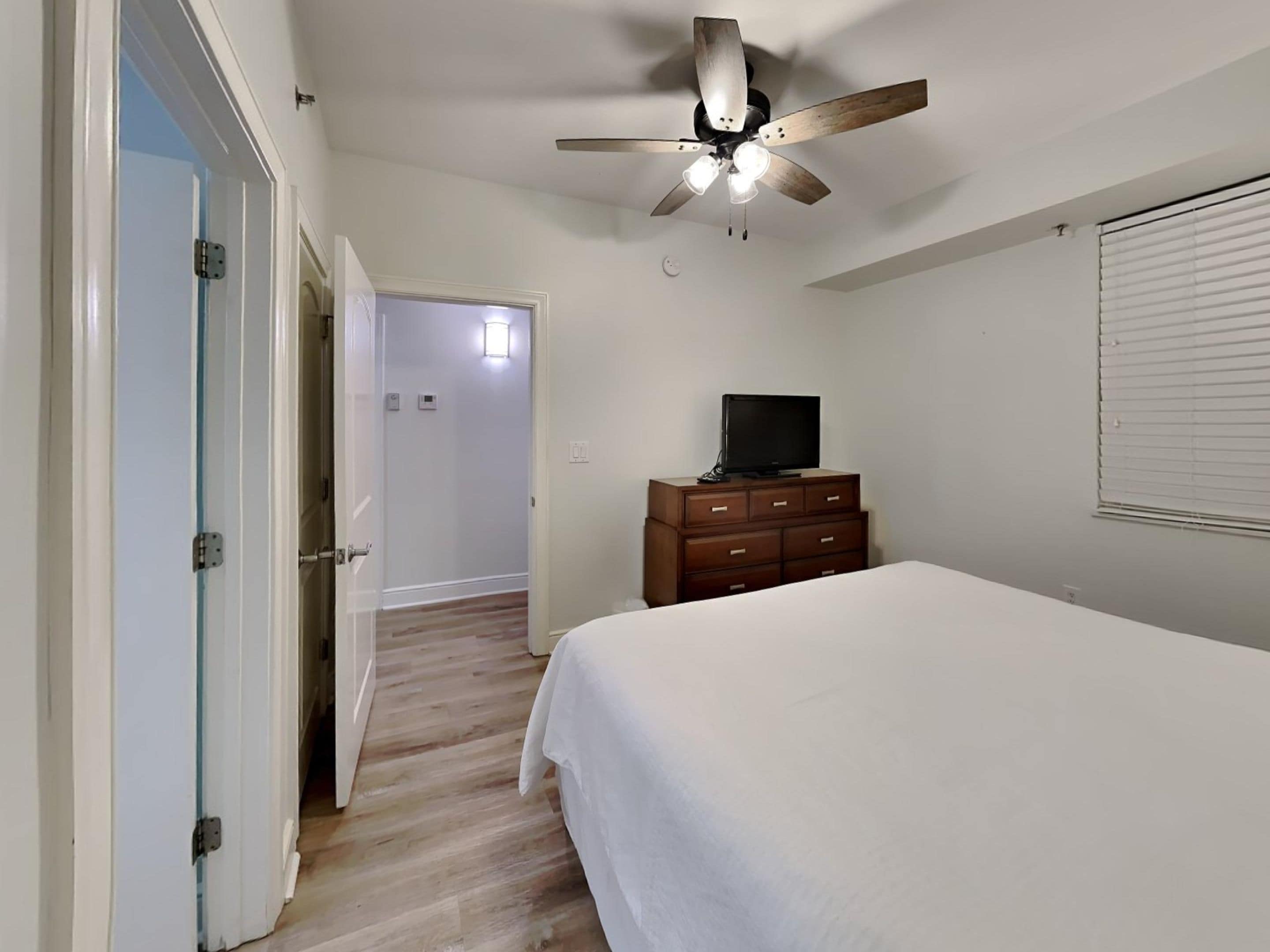 Une chambre à coucher avec un lit, une commode, un téléviseur et un ventilateur de plafond.