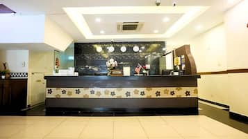 A hotel reception area with a reception desk, a clock, and a plant.