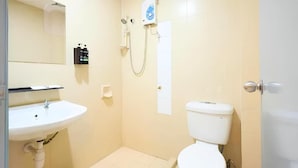 Une petite salle de bain avec un lavabo, des toilettes et une douche, le tout de couleur blanche.