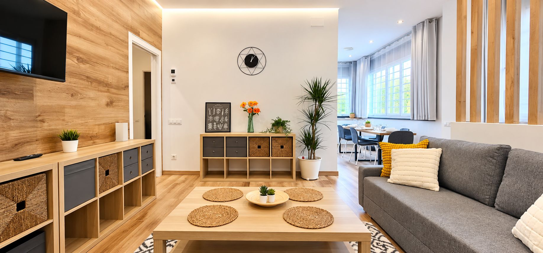 Un salon moderne avec un canapé gris, une table basse en bois et un téléviseur fixé au mur.