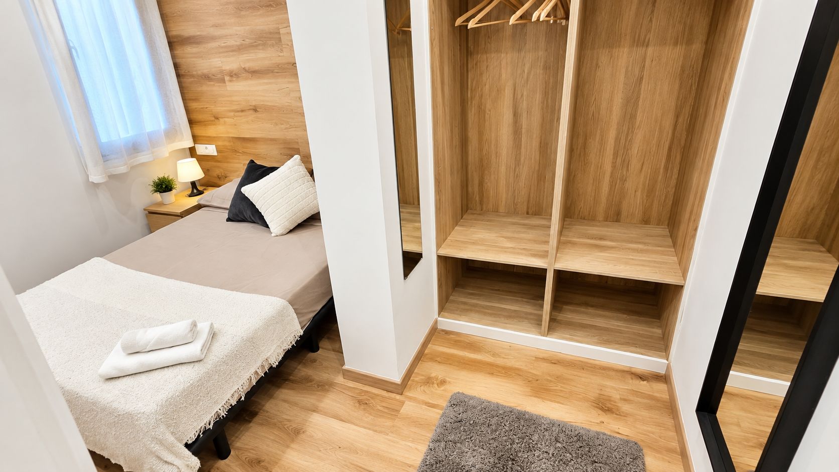 Een slaapkamer met een bed, nachtkastje, lamp en een houten garderobe.