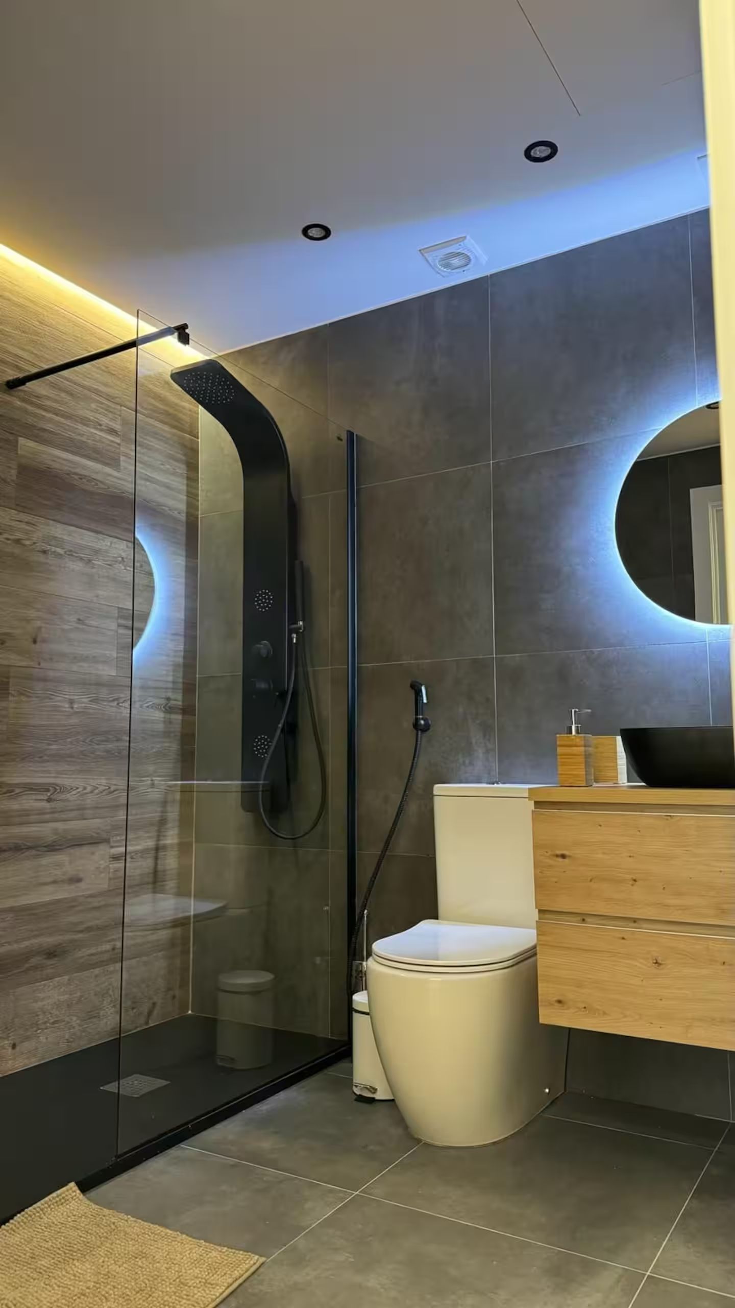 Une salle de bain moderne avec une douche à parois de verre, des toilettes et un meuble-lavabo en bois avec un évier.
