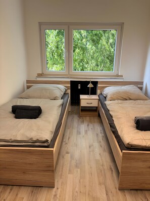 A bedroom with two beds, a nightstand, a lamp, and a window with a view of trees. - 2-bedroom apartment with 5 single beds in Gelsenkirchen (Gelsenkirchen)