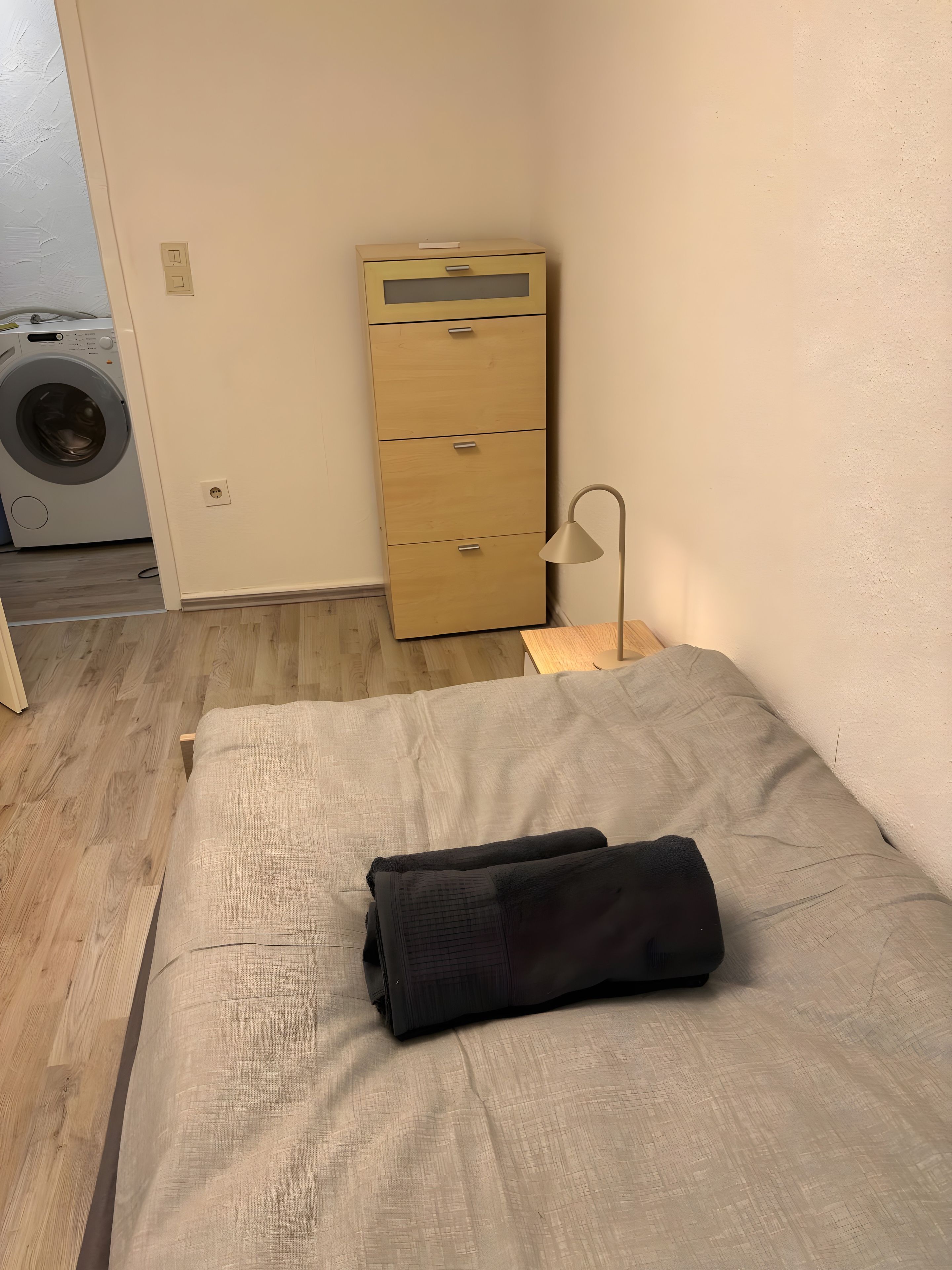 Ein Zimmer mit einem Bett, einem Holzschrank, einer Waschmaschine und einer Lampe.