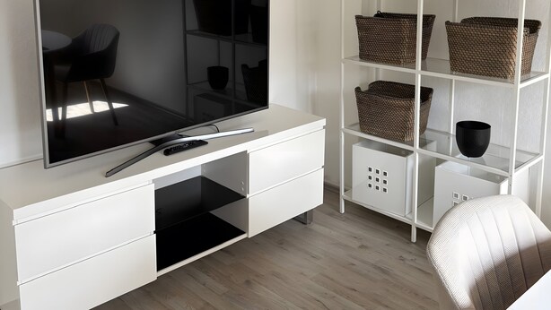 Ein modernes Wohnzimmer mit Flachbildfernseher, weißer Unterhaltungseinheit, Korbwannen und einem hellen Sofa.