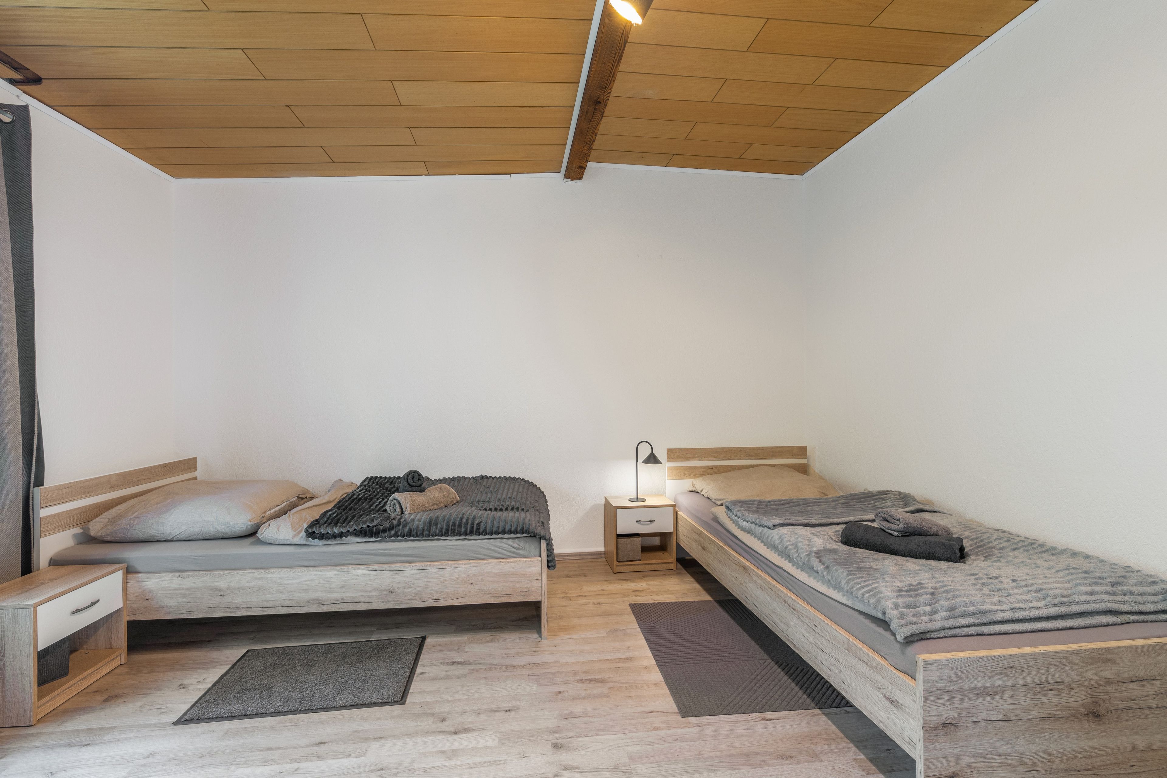 A bedroom with two wooden beds, a nightstand, and a ceiling light.