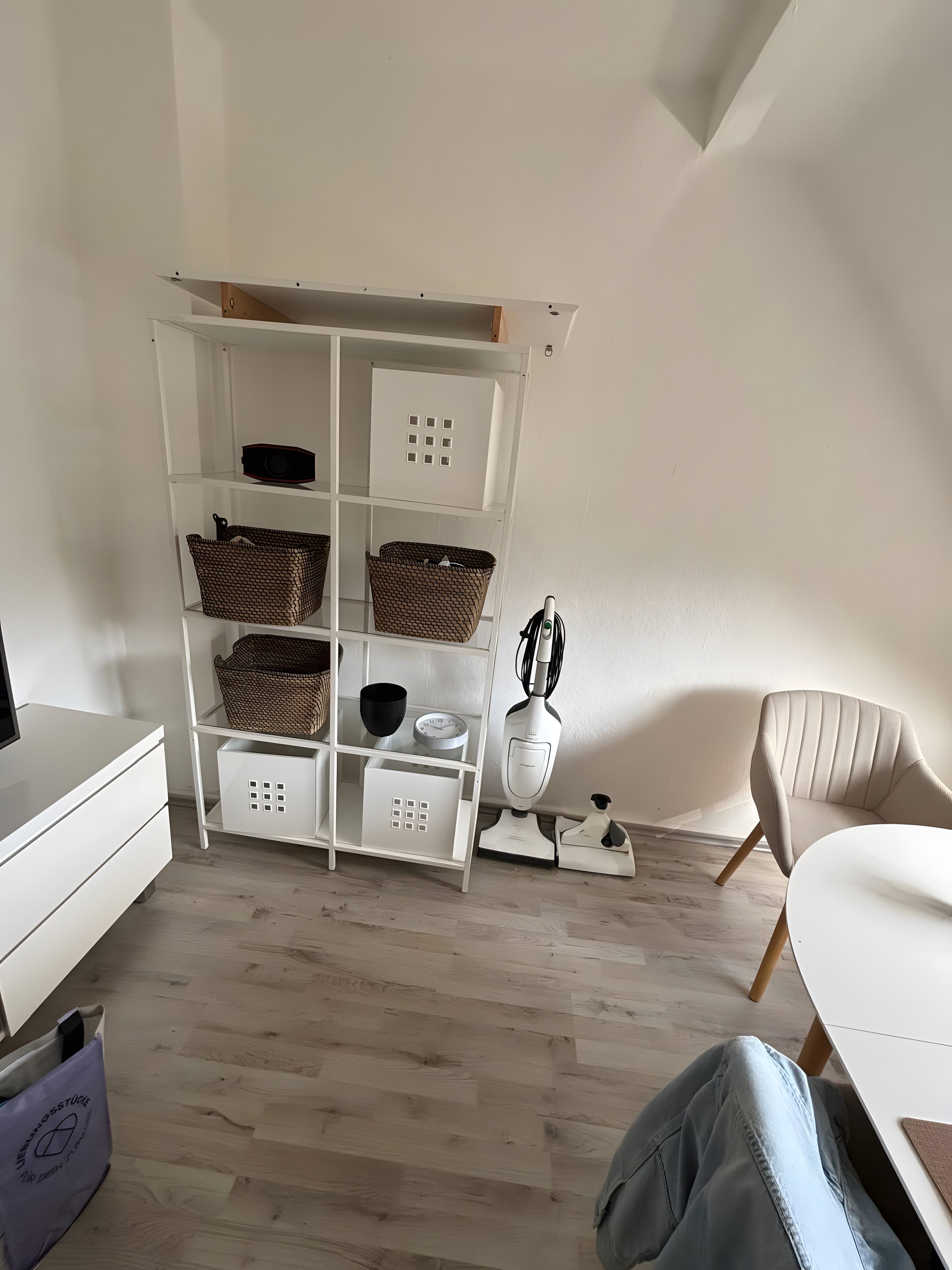 Ein modernes Zimmer mit einer weißen Regaleinheit, einem weißen Tisch, einem weißen Stuhl und einem Holzboden.