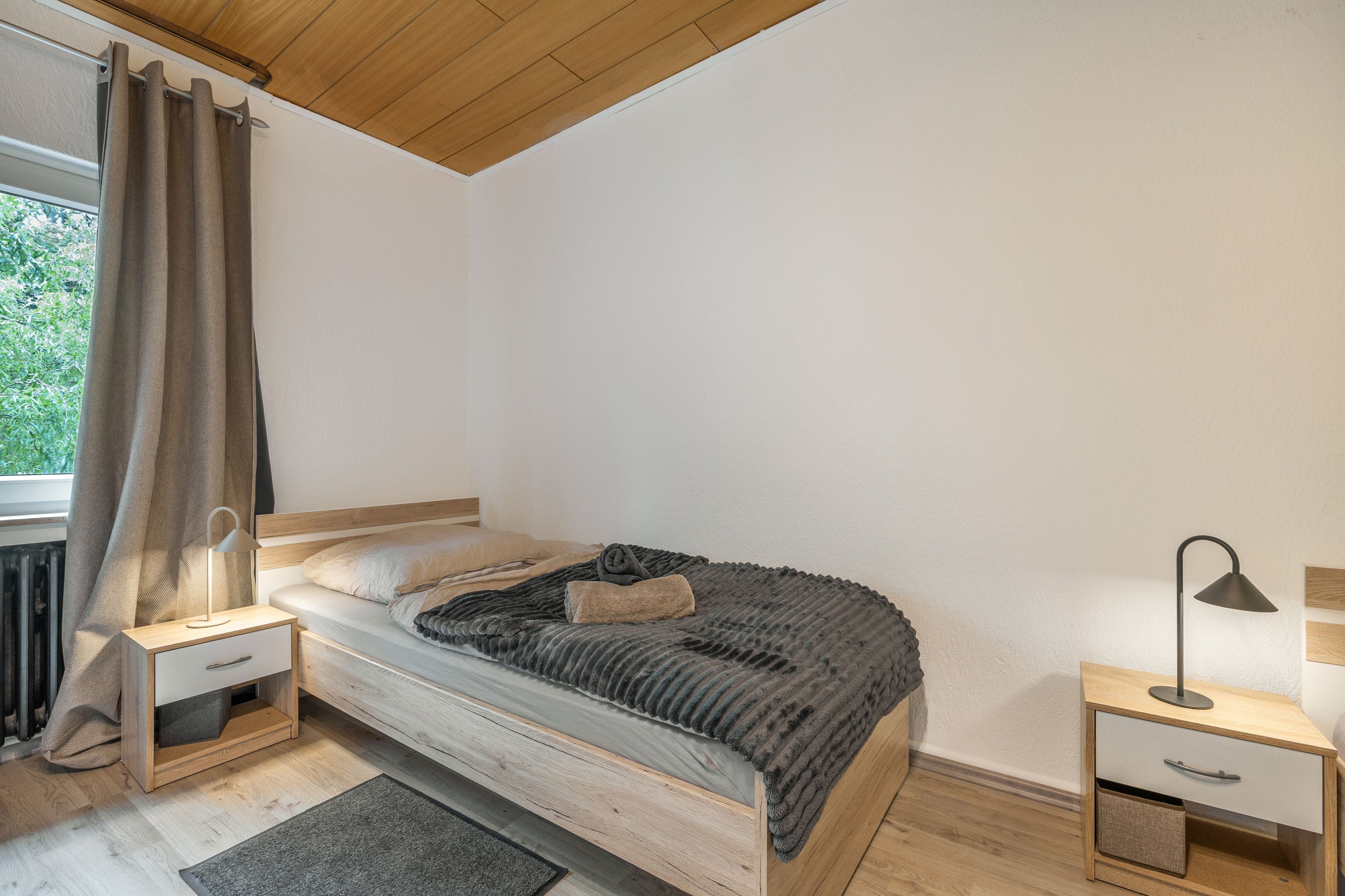 Ein Schlafzimmer mit Bett, Nachttischen, einer Lampe und Blick auf Grünflächen außerhalb.