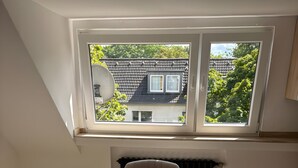 Ein Zimmer mit einem runden Tisch, vier Stühlen, einer Heizung und einem Fenster mit Blick auf Häuser und Bäume.