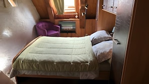 A bedroom with a bed, a chair, and wooden walls.