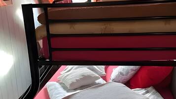 Una cama litera con colchón rojo y almohadas blancas, paredes de madera y una ventana con cortinas.
